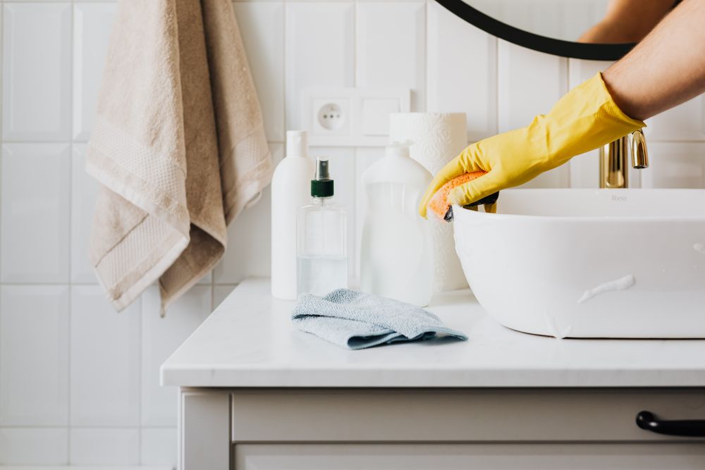 Illustrative stock photo of a gloved hand carefully cleaning a white bathroom basin